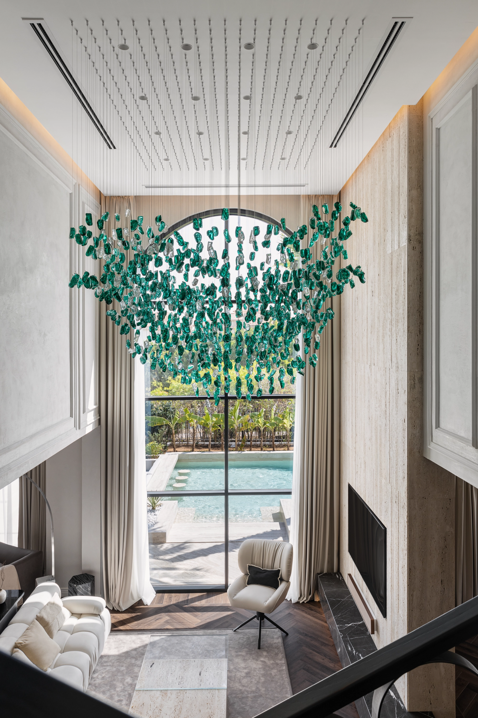 Double-height villa interior with emerald glass chandelier and pool view
